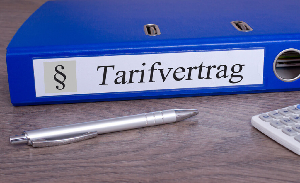 Blauer Ordner mit der Aufschrift Tarifvertrag neben Kugelschreiber und Taschenrechner.