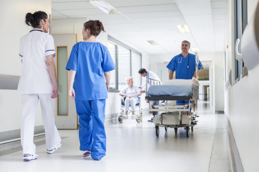 Pflegekr&auml;fte und ein Pfleger mit Patientenbett im Flur einer Klinik.