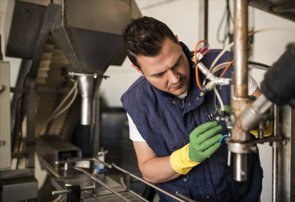 Techniker mit Schutzhandschuhen arbeitet konzentriert an einer Produktionsanlage.