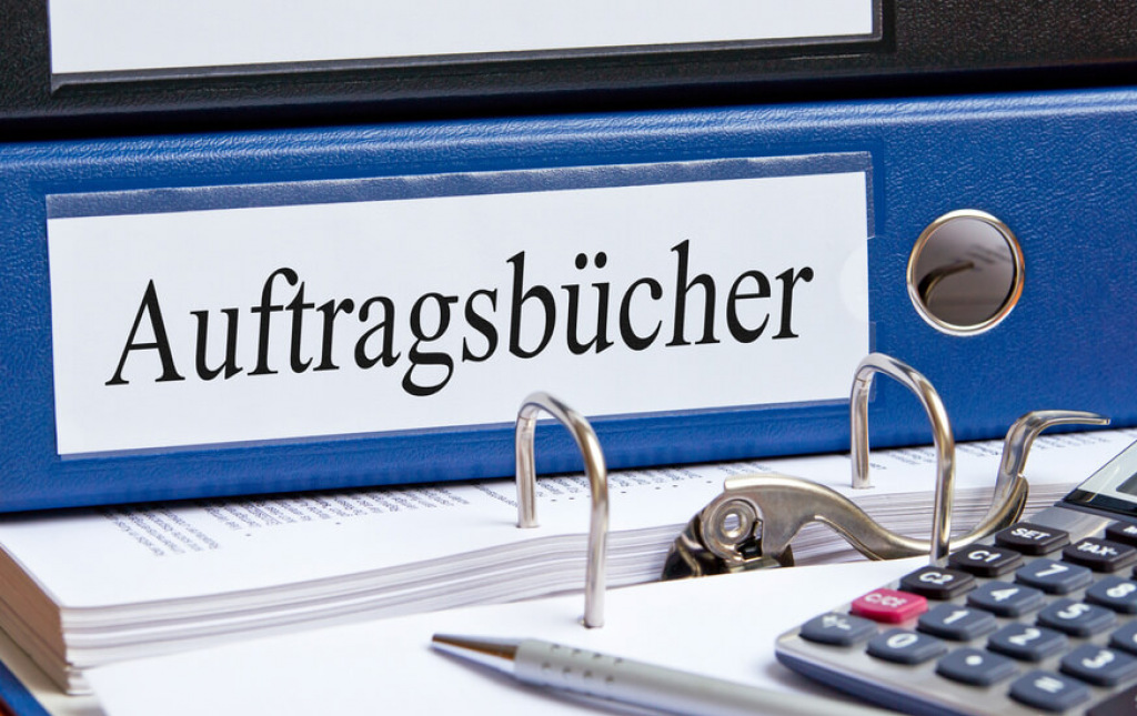 Blauer Ordner mit der Aufschrift Auftragsb&uuml;cher neben Kugelschreiber und Taschenrechner.