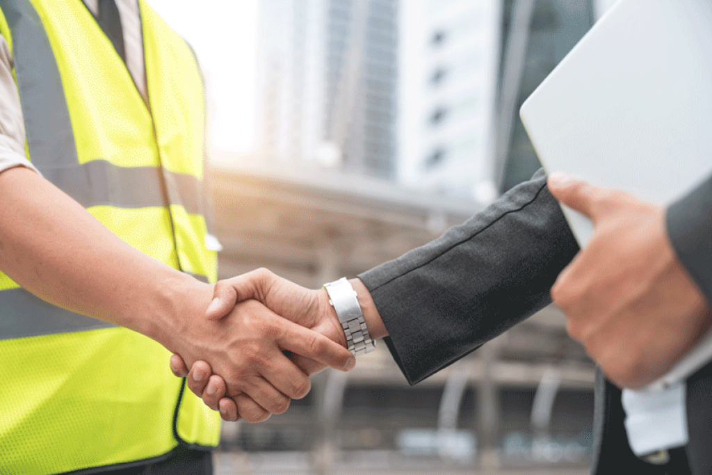 Handschlag zwischen einer Person in Warnweste und einer Person im Anzug auf der Baustelle.